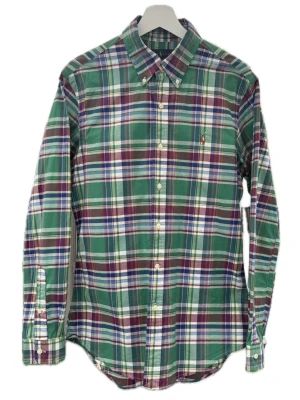 Rutig skjorta från Polo Ralph Lauren - Snygg rutig skjorta från Polo Ralph Lauren i grönt, blått, vinrött och vitt. Skjortan har klassisk krage, knäppning framtill och lång ärm. Broderad logga på bröstet. Perfekt för en stilren look.