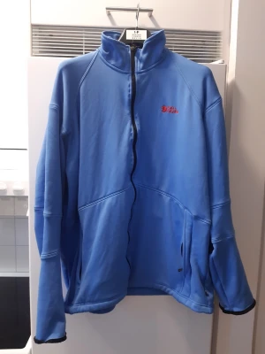 Fjällrävåen fleecetröja /mellanjacka - Säljer en fin Fjällräven-jacka i mycket gott skick, precis som beskrivet. Den är i en härlig blå färg med märkets logotyp på bröstet. Perfekt som ett värmande lager eller som en lätt jacka. Inga fläckar, slitningar eller hål. Så gott som ny.