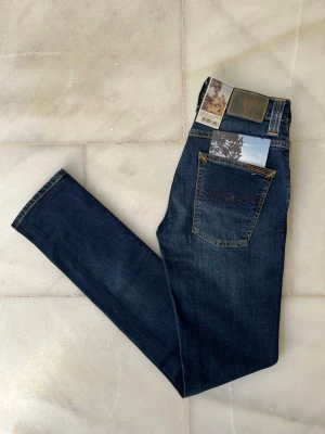 Mörkblå jeans från Nudie Jeans - Väldigt snygga, mörkblå Nudie Jeans med alla tags kvar! Modellen är Grim Tim 😊                          ———————————————————————————                                                     📐| Storlek: 28-32                                                  👖| Märke: Nudie Jeans                                          🔎 | Skick: NYTT SKICK                                          💵 | Ny Pris: 1699kr                                                  ✍🏻 | Skriv om du har några frågor 