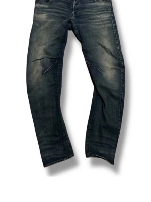 Mörkblå slitna jeans med tvättade detaljer - Säljer ett par mörkblå jeans med snygga slitningar och tvättade detaljer. Jeansen har rak passform och klassisk femficksdesign. Perfekta för en avslappnad och trendig look.