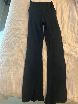 Mörkblåa yogapants från Gina Tricot  - Säljer ett par mörkblåa ribbade leggings från Gina Tricot med hög midja och utsvängda ben. Sköna och stretchiga, perfekta till en avslappnad look. Materialet är mjukt och följsamt, vilket gör dem riktigt bekväma att bära hela dagen.