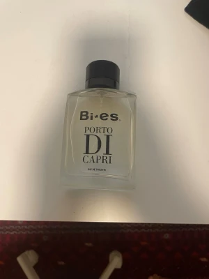 Bi-es Porto Di Capri Eau de Toilette - Fräsch parfym från Bi-es, Porto Di Capri, i en stilren, transparent glasflaska med svart lock och sprayfunktion. Flaskan har en modern, fyrkantig form och tydlig svart text på framsidan. Perfekt för dig som gillar klassiska och eleganta dofter.