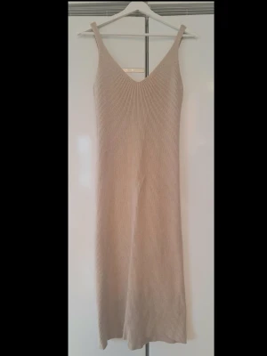 Beige ribbad klänning från Zara S - Säljer en beige ribbad klänning från Zara med smala axelband och v-ringning. Klänningen är figurnära och har en mjuk, stretchig känsla som passar perfekt till varma dagar. Enkel och stilren design som är lätt att matcha.