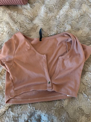 Rosa ribbad croppad topp AsYou - Säljer en ljusrosa croppad topp från AsYou. Toppen är ribbad, har korta ärmar, v-ringning och knappar framtill. Tillverkad i mjuk polyester som sitter skönt på kroppen. Perfekt för dig som gillar trendiga och bekväma plagg.