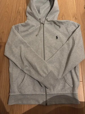 Ljusgrå hoodie från Ralph Lauren - En grå zip hoddie från Ralph lauren. Har en defekt på handleden och där med pris lågt.