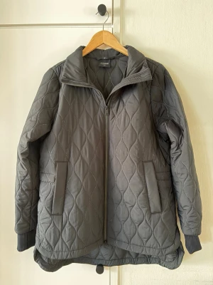 Svart quiltad jacka från Everest - Svart quiltad jacka från Everest med dragkedja framtill, två fickor och ribbade muddar vid ärmsluten samt dragsko i ryggen. Jackan är lätt vadderad. Väldigt fint skick. Köpt på Vinted men passade inte mig. 