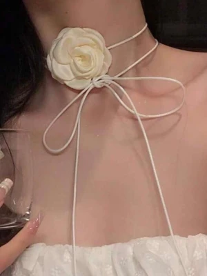 Choker med creamfärg  ros och band - Supersnygg choker med en stor vit tygros framtill och tunna vita band som knyts i en rosett runt halsen. Perfekt för att ge din outfit en romantisk och trendig touch. Rosetten och blomman ger ett unikt och elegant uttryck.