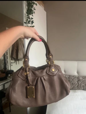 Brun Marc Jacobs handväska i läder - Brunbeige väska från Marc Jacobs i läder med guld detaljer. Rymlig och som i nyskick💕