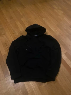 Svart hoodie med dragsko - Svart hoodie från Polo Ralph Lauren med klassiska broderade loggan på bröstet. Stilren och tidlös modell som passar till allt.  • Färg: svart • Skick: mycket Bra skick (använd lite men väl omhändertagen) • Passform: Normal • Material: Mjuk och bekväm bomullsblandning Perfekt för både vardag och chill outfits Säljs då den inte används längre.  Skicka meddelande vid frågor eller för fler bilder!