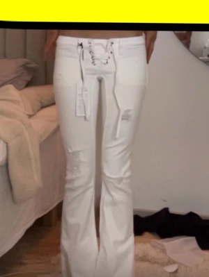 Gina slutsålda jeans  - storlek xxs tall!! Säljer ett par vita bootcut jeans med snörning i midjan och slitna detaljer på låren och knäna. Jeansen har fickor fram och en snygg, trendig passform som ger en cool vibe. Perfekta för dig som vill sticka ut med din stil.