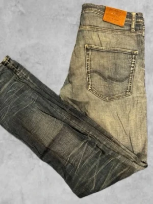 Slim fit jeans från Jack Jones  Jeans - Säljer ett par snygga slim fit jeans från Jack Jones Jeans i tvättad gråblå denim. Jeansen har klassisk femficksmodell, kontrastsömmar och läderpatch bak i midjan. Materialet är bomull med stretch för extra komfort. Perfekta för en avslappnad och trendig look.