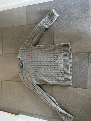Grå kabelstickad tröja Polo Ralph Lauren - Sjukt Fet Kabelstickad Ralph lauren tröja. Den är i väldigt bra skick och använd 3-6 ggr. Säljer den pga är för liten, och storlek är S, Jag är ca 170 och lite för liten för mig. Pris kan diskuteras.
