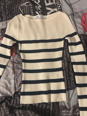 Randig ribbad tröja från ZARA - Säljer en krämvit ribbad tröja från ZARA med mörkblå horisontella ränder. Tröjan har lång ärm, rund halsringning och är figurnära i modellen. Perfekt för dig som gillar en klassisk men trendig look.