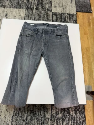 Grå jeans från Jack & Jones - Snygga grå jeans från Jack & Jones med klassisk femficksdesign och raka ben. Jeansen har en tvättad look och är tillverkade i ett mjukt denimtyg som ger en avslappnad vibe. Perfekta till sneakers och hoodie för en chill stil.