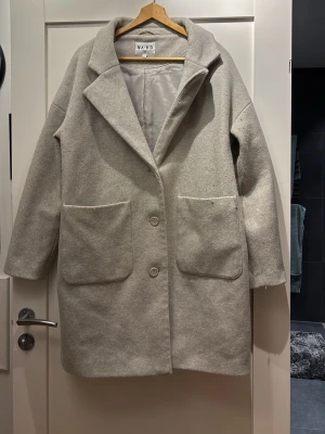 Ljusgrå/beige kappa från NA-KD - Stilren ljusgrå kappa från NA-KD med två stora framfickor och klassisk krage. Perfekt för kyliga dagar och enkel att matcha med olika outfits. Välanvänd och nopprig, se bild 3❣️