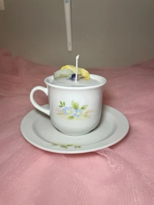 Doftljus med vaniljdoft i en tekopp med fat med blommig design  - Det här ljuset är gjort av återanvändbara material. Tekoppen är köpt secondhand och stearinet är från kyrkor som tänkte slänga det. Det här ljuset har en svag doft utav vanilj, så känsliga även kan använda det. Det här ljuset har även torkade blommor på som dekoration. 