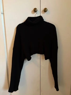 Svart cropped polotröja stickad - Säljer en svart stickad cropped polotröja med långa ärmar. Tröjan har en hög, vikt krage och är ribbstickad för extra struktur. Perfekt för lager på lager och en trendig look. (Väldigt kort)