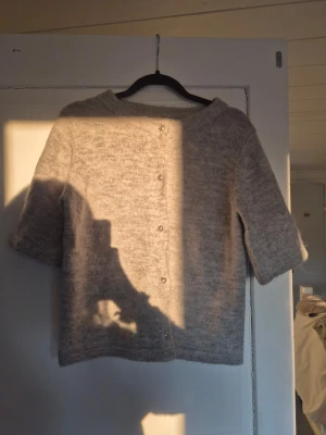 Ljusgrå stickad tröja med knappar - Mysig ljusgrå stickad tröja med rund hals och halvlånga ärmar. 