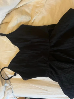 Svart linne med volang  - Snygg svart volang linne från SHEIN med tunna axelband och lätt ribbad struktur. Linnet har en enkel och stilren design som passar perfekt till många olika tillfällen.