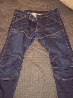 Mörkblå jeans med kontrastsömmar - Säljer ett par mörkblå jeans med coola kontrastsömmar och unika fickdetaljer både fram och bak. Jeansen har en modern passform och är tillverkade i slitstark denim. Perfekta för dig som gillar en streetig och avslappnad stil.