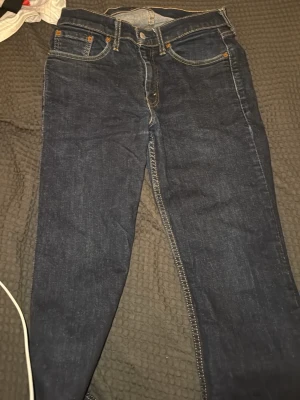 Mörkblå raka jeans från Levi's - Snygga mörkblå jeans från Levi's med klassisk femficksmodell och raka ben. Jeansen har kontrastsömmar och en liten röd Levi's-lapp på bakfickan. Tillverkade i slitstarkt denimtyg som ger en tidlös look.