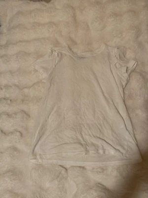 Vit basic t-shirt från Vero Moda - En enkel vit t-shirt från Vero Moda med klassisk rund hals och korta ärmar. Tillverkad i mjuk bomull, perfekt för en clean och avslappnad stil. Passar till allt och är ett måste i garderoben. Lite genomskinlig. 