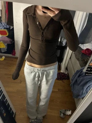 Brun ribbad långärmad topp - Säljer en brun ribbad långärmad topp med v-ringning och knappar framtill. Toppen har en klassisk krage och sitter tight mot kroppen för en snygg siluett. Perfekt att styla med jeans eller kjol för en trendig look.