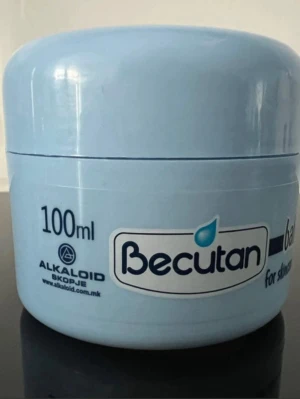 Becutan babykräm 100ml - Ljusblå burk med Becutan babykräm, 100 ml. Krämen är framtagen för hudvård och skydd, speciellt anpassad för känslig hud. Burken är rund och tillverkad i plast, med tydlig märkning och illustration av en bebis på etiketten.