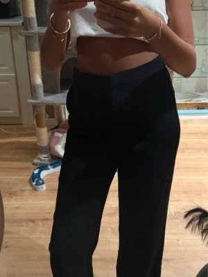 Svarta vida kostymbyxor - Snygga svarta kostymbyxor med hög midja och raka, vida ben. Byxorna har en klassisk look med diskret knapp och dragkedja framtill. Perfekta att styla med crop top eller skjorta för en trendig vibe.