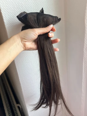 Mörkbrunt clip-on löshår - Säljer ett set mörkbrunt clip-on löshår från rapunzelofswe. Löshåret är av naturligt hår och är i färgen chocolate brown. 40 cm, 7 delar. Aldrig använt. Köpt för 1600 ink frakt. Säljer för 1000