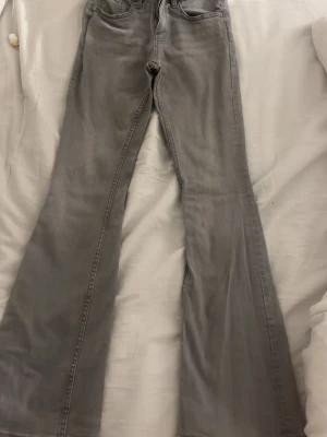 Grå bootcut jeans med utsvängda ben - Säljer ett par grå jeans med bootcut-modell och utsvängda ben. Klassisk femficksdesign och normal midja. Jeansen är i ett mjukt denimtyg som ger en avslappnad look. Perfekta för dig som gillar retrostil och vill ha något bekvämt men ändå trendigt.