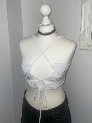 Vit croppad linnetopp med snörning - Trendig vit croppad linnetopp med smala axelband och snygg snörning framtill. Toppen har ett ringformat hål under bysten och omlottband som korsas över bröstet. 