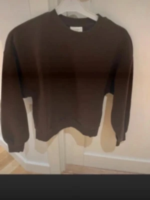 Mörkbrun sweatshirt med rund hals - En enkel och stilren mörkbrun sweatshirt med rund halsringning och långa ärmar. Tröjan har ribbade muddar vid ärmslut och nederkant, perfekt för en avslappnad och trendig look. Passar till både jeans och mjukisbyxor.så perfekt 