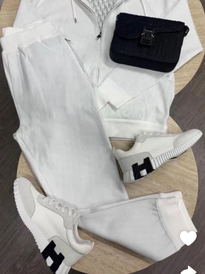 Bundle allt tillsammans  - Snygg vit hoodie från Dior med dragkedja framtill och diskret logga på bröstet. Hoodien har en huva med dragsko och ribbade muddar vid ärmslut och nederkant. Perfekt för en clean och exklusiv streetwear-look.