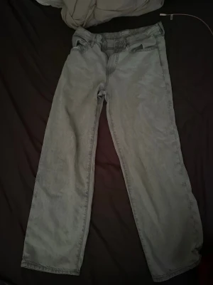 Ljusgrå loose fit jeans - Ljusgrå jeans med loose fit och raka ben. Klassisk femficksdesign och knappgylf. Materialet är denim, vilket ger en cool och avslappnad look. Perfekt för dig som gillar en bekväm och trendig stil.