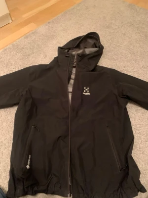 Svart vindjacka från Haglöfs !pris kan diskuteras! - Säljer en svart vindjacka från Haglöfs i dammodell, storlek L, vilket jag skulle säga är motsvarande S i herrstorlek. Damstorleken ger en bättre passform tycker jag. Jackan har huva, dragkedja framtill och två sidofickor med dragkedja. Tillverkad i slitstark polyester med meshfoder och GORE-TEX-detaljer för extra skydd mot väder. Köpt för 3000kr pris är ej hugget i sten. Använd max 10 gånger