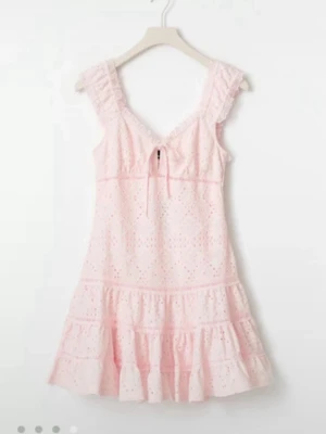 Ljusrosa spetsklänning med volang - Söt ljusrosa kortklänning med broderad spets, volangdetaljer och v-ringning med knyt framtill. Klänningen har breda axelband och en luftig, feminin siluett som passar perfekt till sommaren.