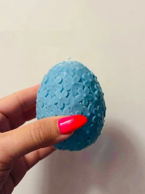 Blå äggformad ljusdekoration - Säljer ett äggformat ljus i blått med blommönster över hela ytan. Ljusets yta är täckt av små, upphöjda blommor och det kommer i en ljusrosa presentask med fönster. Perfekt som dekoration eller present.