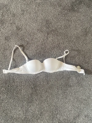 Vit push-up bh med justerbara band - Säljer en vit push-up bh med vadderade kupor och justerbara axelband. Bh:n har slät design utan spets eller mönster och stängs med hyskor bak. Perfekt för dig som vill ha en enkel och stilren bh under alla typer av plagg.
