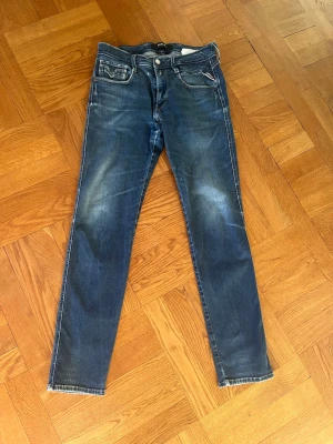 Blåa Replay jeans - Riktigt snygga blåa slim fit jeans från Replay med slitningar och klassiska fem fickor och detaljerade sömmar, storlek 32/32. Materialet är mjukt denim med stretch för extra komfort. Inga defekter