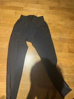 Svarta träningsbyxor från Under Armour - Svarta träningsbyxor från Under Armour med dragkedjeförsedda fickor och smal passform. Byxorna har en diskret logga på låret och är tillverkade i ett stretchigt funktionsmaterial som passar perfekt för träning och sport.