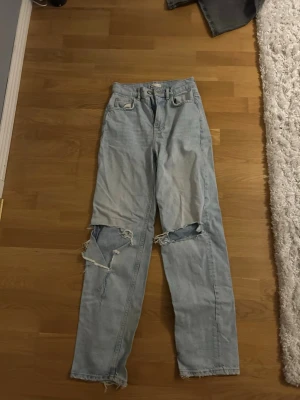 Ljusblå ripped jeans från g perfect jeans - Säljer ett par högmidjade ljusblå jeans från g perfect jeans i storlek 32. Modellen har raka ben, slitna detaljer och stora hål vid knäna för en edgy look. Klassisk femficksdesign och fransiga benslut. Perfekt för dig som gillar streetstyle. Säljer då den ej används längre