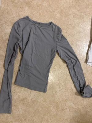 Grå långärmad topp - En enkel och stilren grå långärmad topp med rund hals. Toppen har en slim passform och är tillverkad i mjukt bomullsmaterial, perfekt att matcha med jeans eller kjol för en clean look.