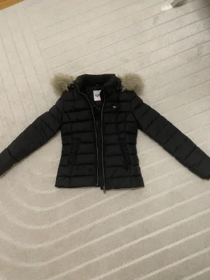 Svart pufferjacka Tommy Jeans XS - Säljer en svart pufferjacka från Tommy Jeans i storlek XS. Jackan har huva med fuskpäls, dragkedja framtill och två fickor med dragkedja. Tillverkad i polyester och perfekt för kalla dagar. Snygg, enkel och riktigt skön att bära.