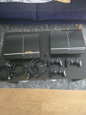 PlayStation 3 konsoler med tillbehör - Två svarta PlayStation 3-konsoler från Sony med tillhörande strömkablar, HDMI-kablar och tre trådlösa DualShock 3-handkontroller. Konsolerna har en stilren, blank finish och klassisk rektangulär form. Perfekt för gaming och filmkvällar. Ps3 fungerar utmärkta och har inga konstigheter bara handkontroller är lite sliten och har dryft 
