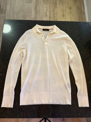 Loro piana polo - Klassisk vit långärmad tröja från loro piana  med krage och två knappar vid halsen. Tillverkad i ett tunt, mjukt material som känns lyxigt och passar perfekt till en stilren look. Enkel design med ribbade muddar och diskret elegans.