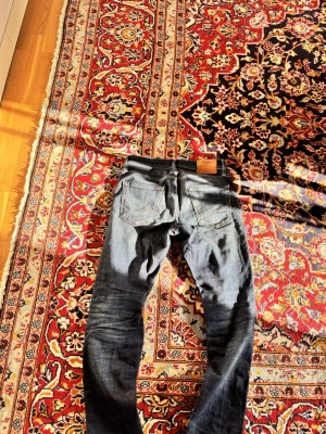 Svarta slim fit jeans med slitningar - Snygga svarta slim fit jeans med slitningar och tvättade detaljer. Klassisk femficksmodell med dragkedjegylf och läderpatch bak i midjan. Perfekta för en trendig och avslappnad look.