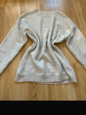 Beige stickad tröja Gina Tricot - Mysig beige stickad tröja från Gina Tricot med rund halsringning och långa ärmar. Tröjan har ribbade muddar vid hals, ärmslut och nederkant. Perfekt för lager på lager och enkel att matcha till olika outfits.