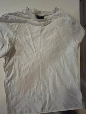 Vit basic t-shirt i bomull - H&M - En enkel vit t-shirt med rund hals och korta ärmar. Tillverkad i mjuk bomull, perfekt för en clean och avslappnad stil. Passar till det mesta och är ett måste i garderoben.