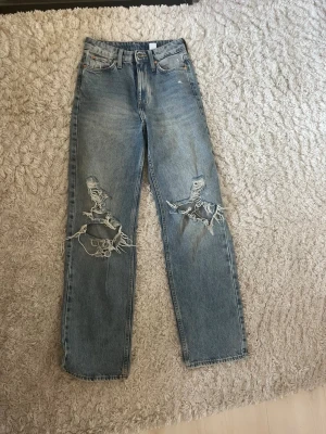 Blåa ripped jeans med hög midja - Säljer ett par blåa raka jeans med hög midja och stora slitningar över knäna. Jeansen har klassisk femficksmodell och är i ett kraftigt denimtyg. 
